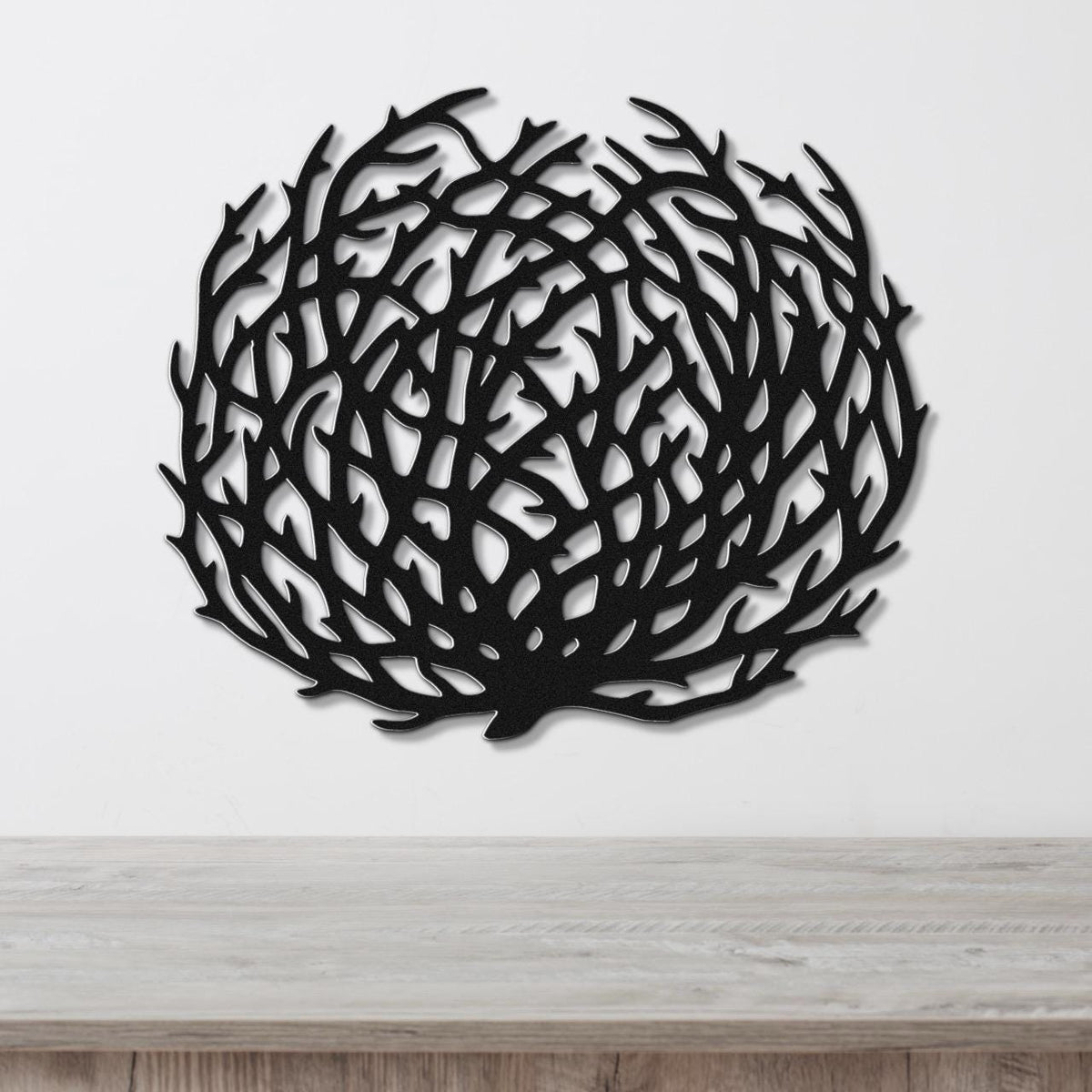 Black metal tumbleweed wall art with intricate branch cutouts, mounted on a white wall above a light wood counter.