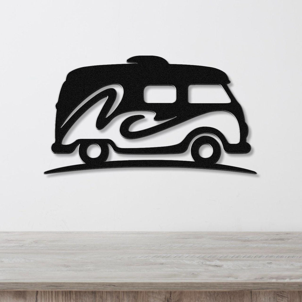 Black metal wall art silhouette of a vintage camper van with a wave design, mounted on a white wall above a wooden surface.