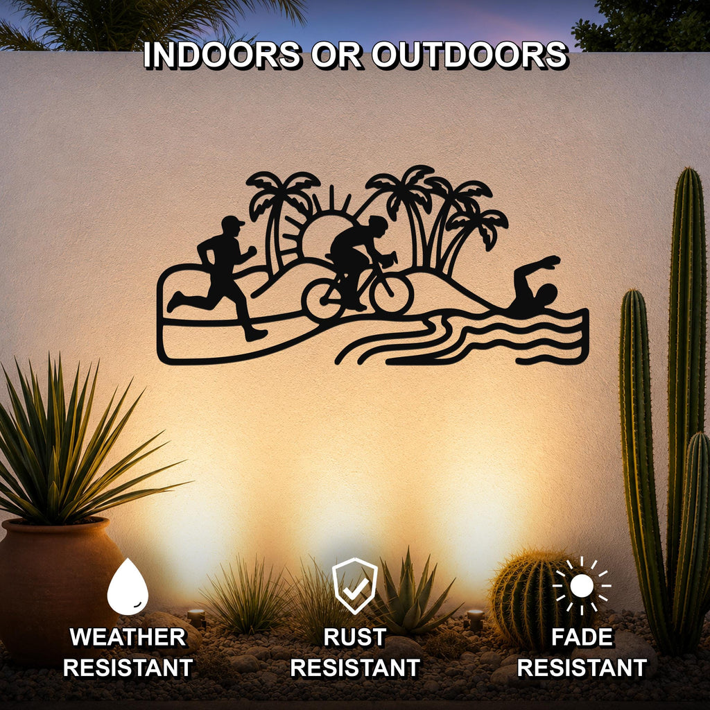 Black metal triathlon wall art with swim, bike, and run silhouettes, palm trees, and waves, mounted on an outdoor wall above a desert garden with cacti.