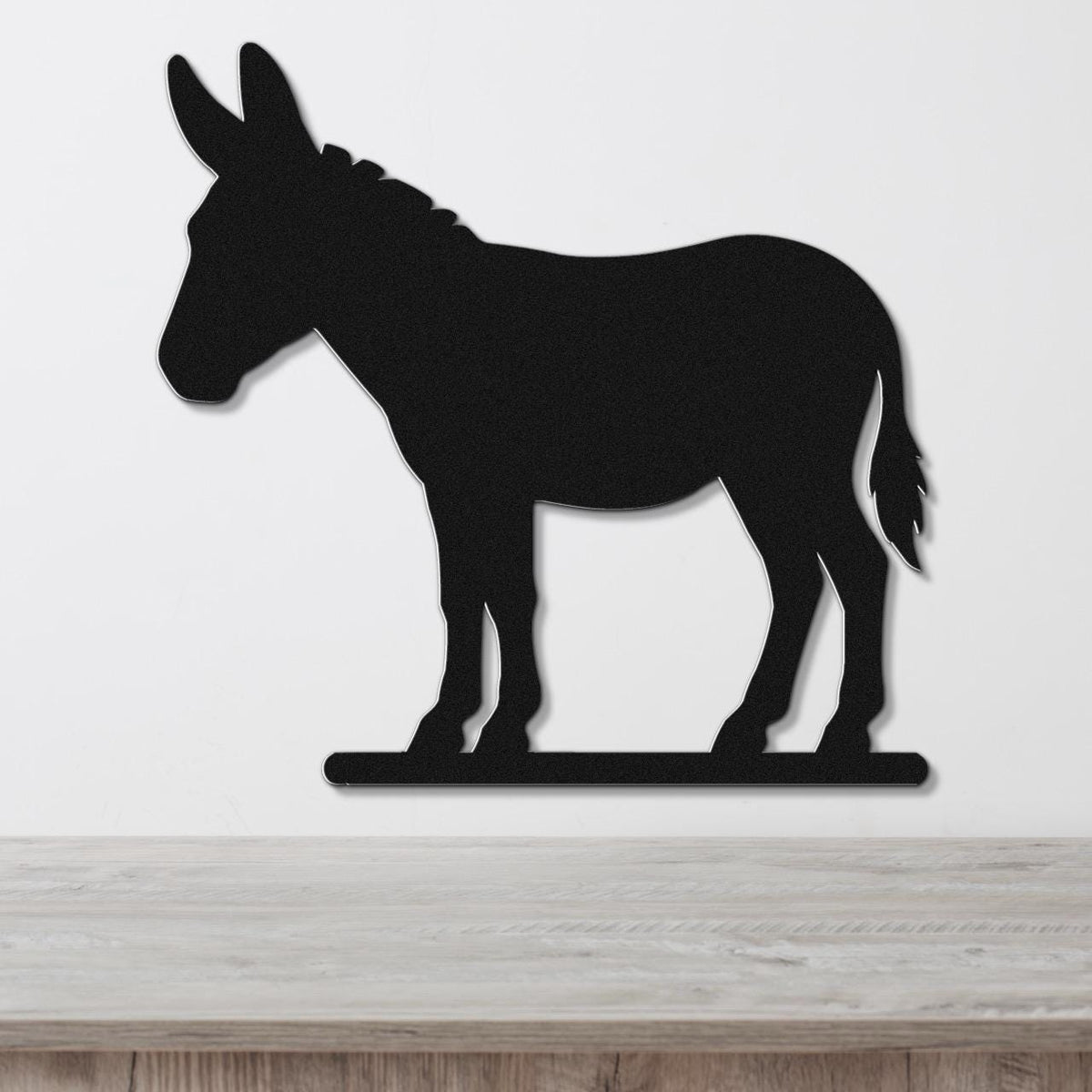Black metal donkey wall art silhouette with a textured finish, mounted on a white wall above a light wood surface.