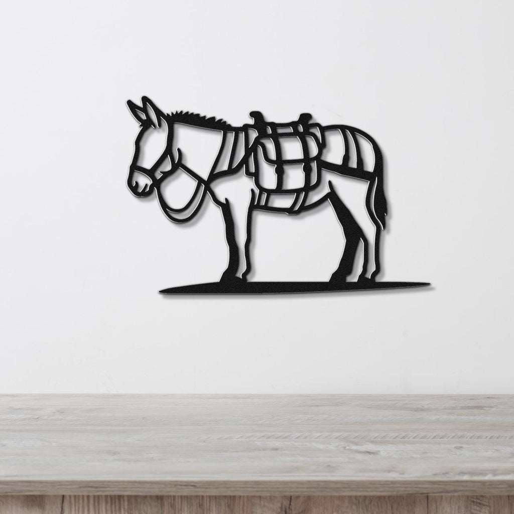 Black metal burro wall art with saddle and harness cutouts, mounted on a white wall above a wooden surface.