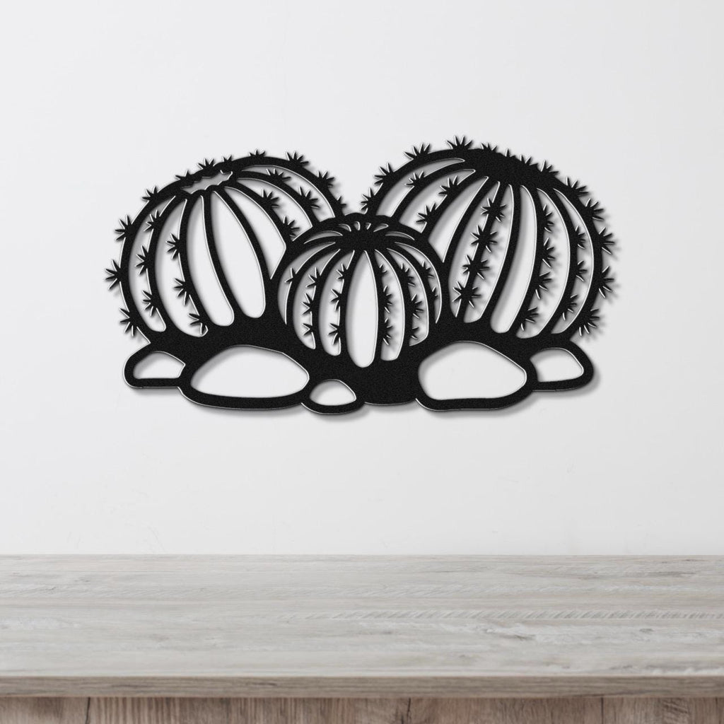 Black metal barrel cactus wall art with spines and vertical ribs cutout, mounted on a white wall above a wooden surface.