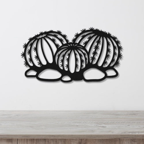 Black metal barrel cactus wall art with spines and vertical ribs cutout, mounted on a white wall above a wooden surface.