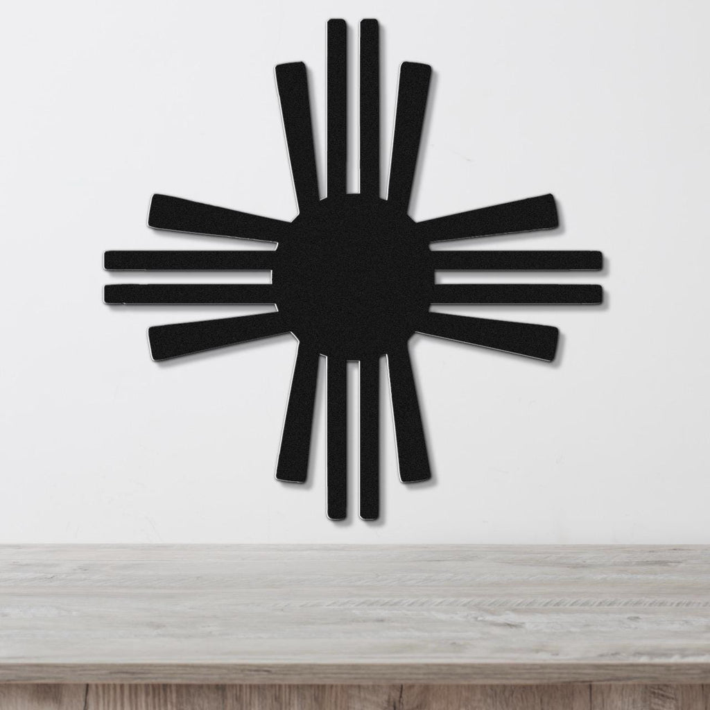 Black metal Zia Sun symbol wall art with radiating rays, mounted on a white wall above a light wood surface.