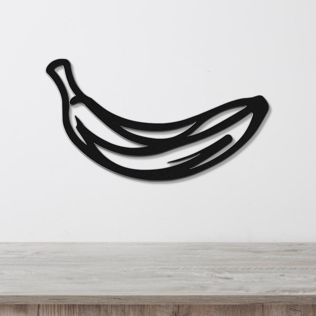 Black metal banana wall art with internal cutout lines, mounted on a white wall above a light wood countertop.