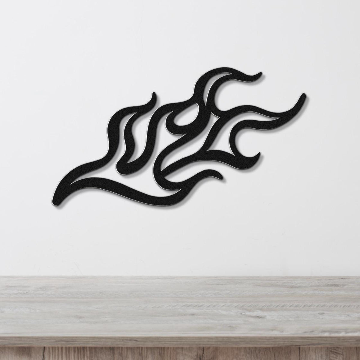 Black metal wall art with a fluid flame design, featuring interwoven curves and cutouts, mounted on a white wall above a light wood surface.