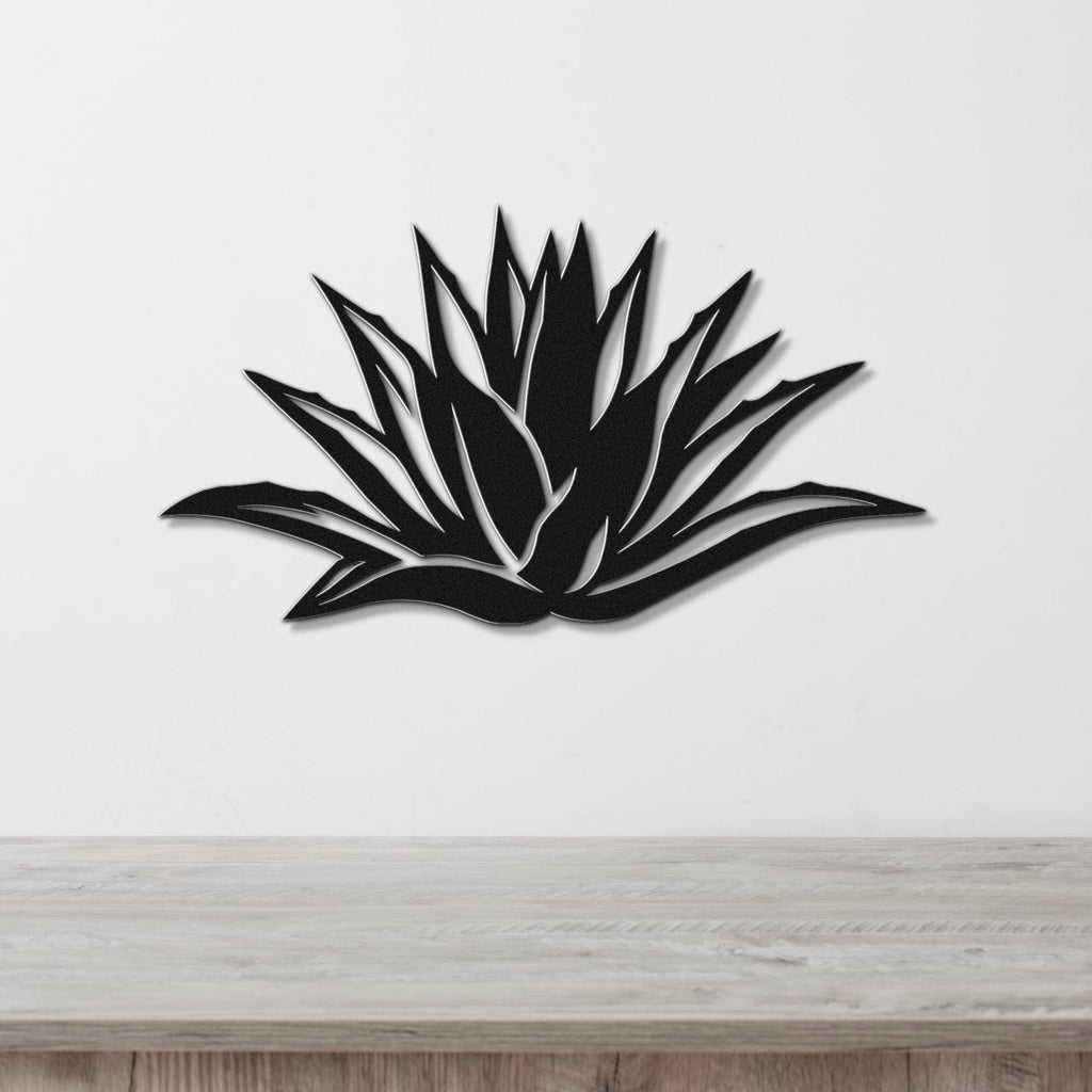 Black metal agave wall art with sharp, pointed leaf cutouts, mounted on a white wall above a light wood surface.