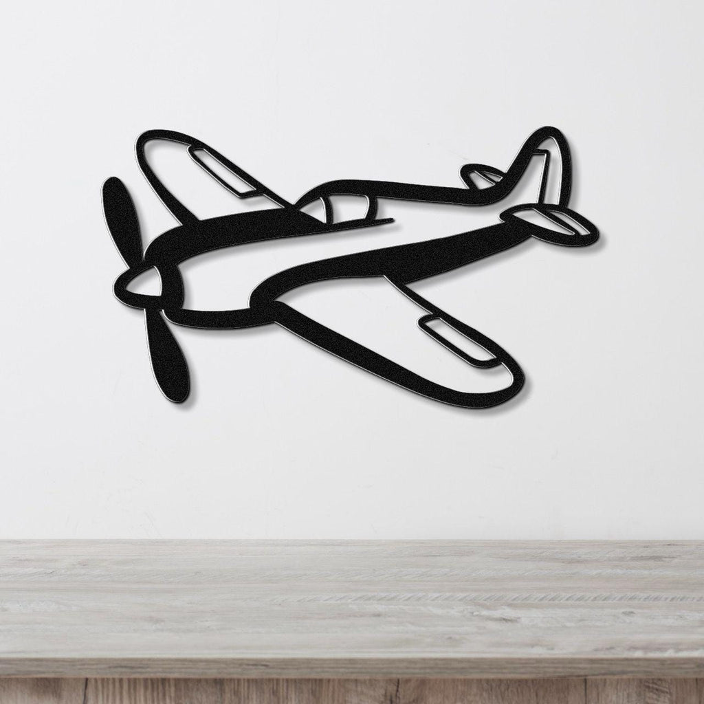 Black metal airplane wall art with a bold silhouette design, featuring cutout details of the propeller and cockpit, mounted on a white wall above a wooden surface.