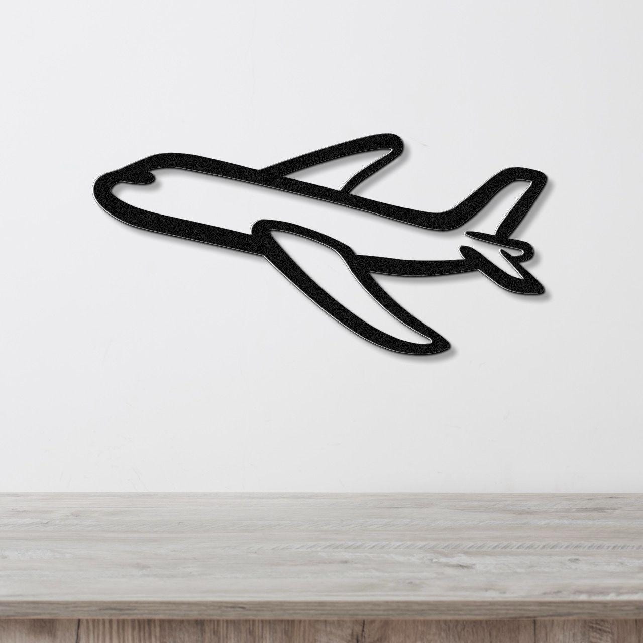 Black metal airplane wall art with a bold silhouette design, mounted on a white wall above a light wood surface.