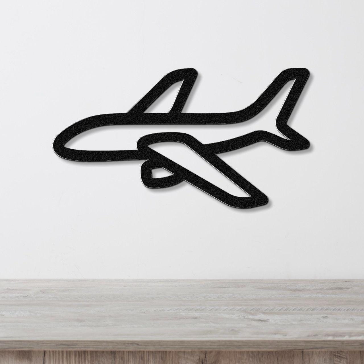 Black metal airplane wall art with a silhouette cutout design, mounted on a white wall above a light wood surface.