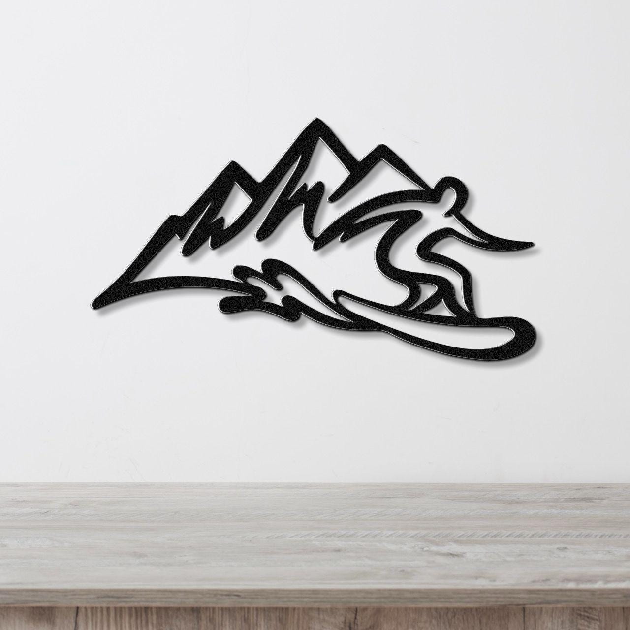 Black metal wall sculpture of a snowboarder in motion with mountain silhouette, mounted on a white wall above a wooden counter.