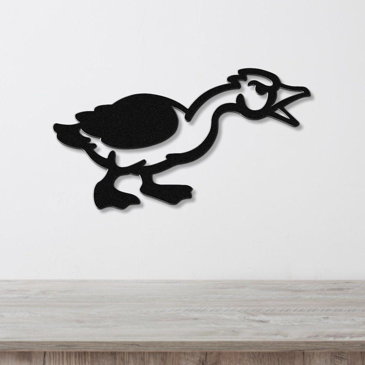 Black metal wall art silhouette of a goose in motion, mounted on a white wall above a light wood surface.