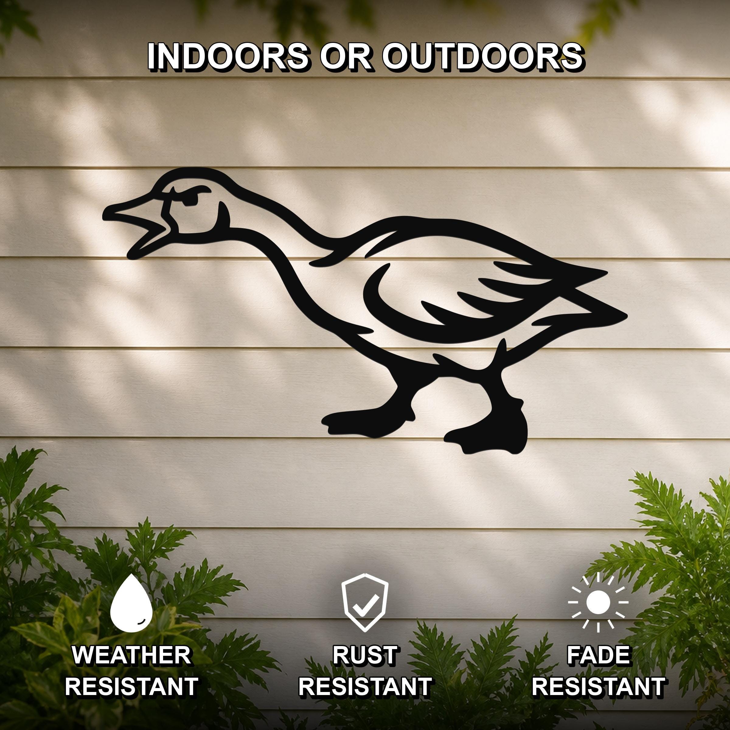 Black metal goose wall art silhouette with an angry expression, mounted on a beige outdoor wall with green plants below, weather resistant, rust resistant, and fade resistant.