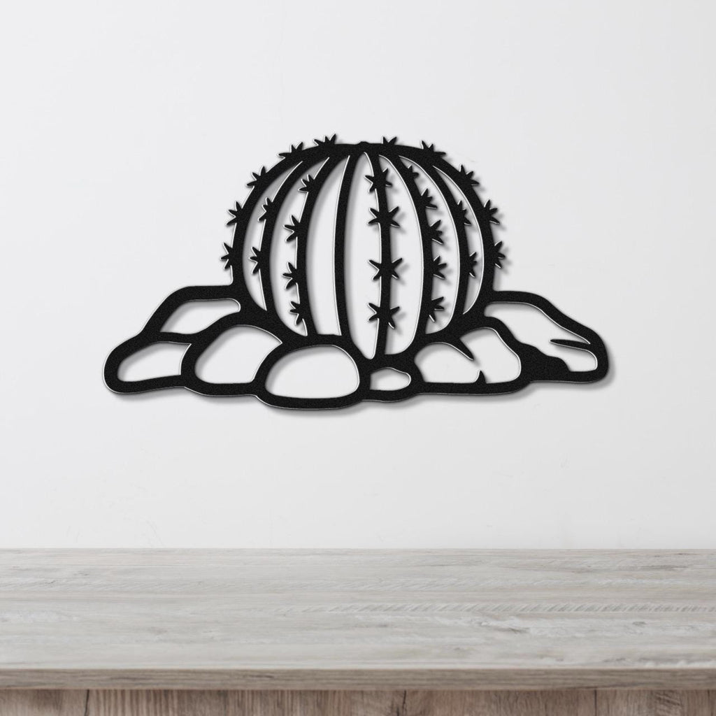 Black metal barrel cactus wall art with spines and rocks cutout, mounted on a white wall above a wooden counter.