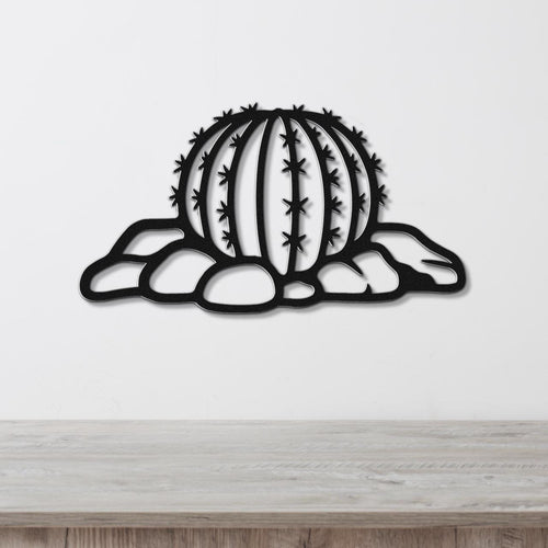 Black metal barrel cactus wall art with spines and rocks cutout, mounted on a white wall above a wooden counter.