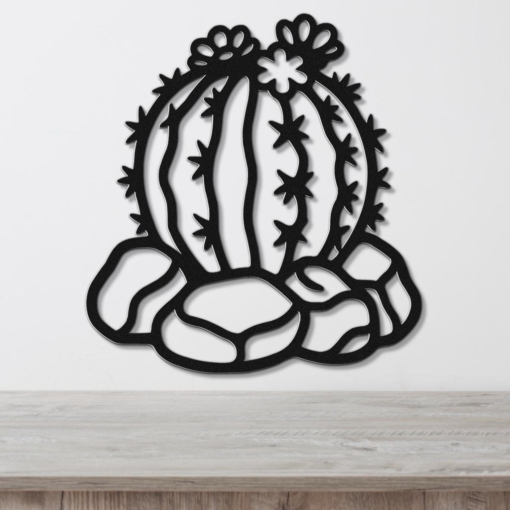 Black metal barrel cactus wall art with flower and spine cutouts, mounted on a white wall above a wooden surface.