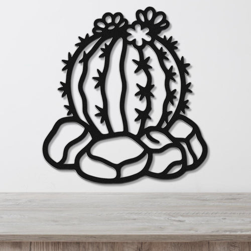 Black metal barrel cactus wall art with flower and spine cutouts, mounted on a white wall above a wooden surface.