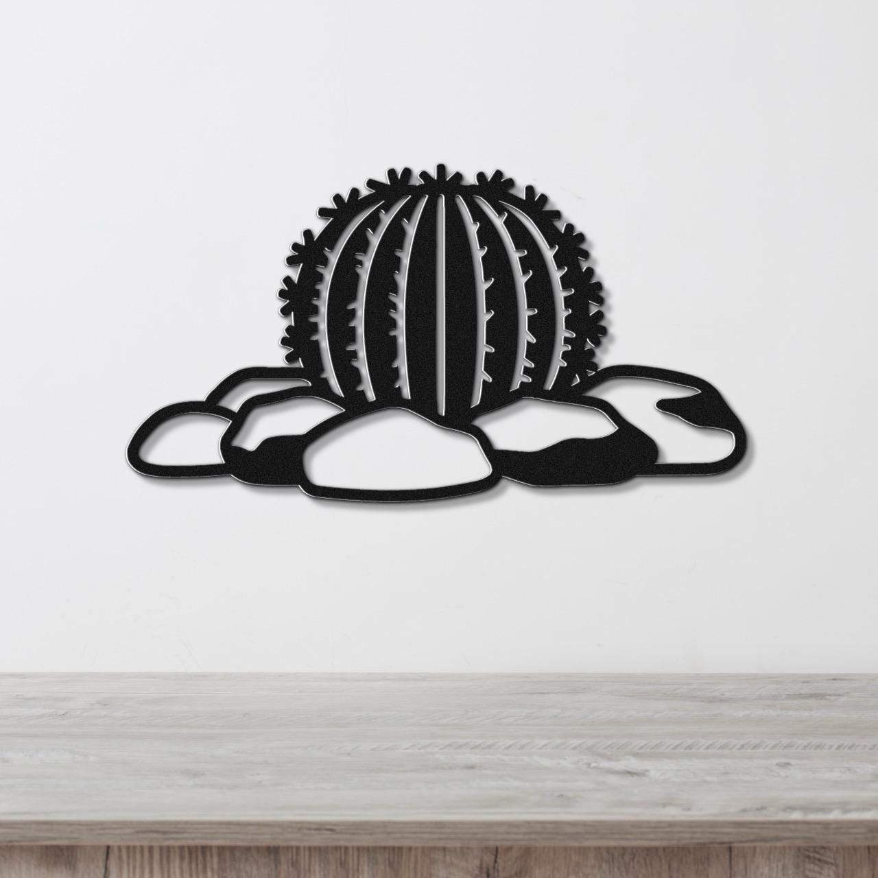 Black metal barrel cactus wall art with spines and rocks cutout, mounted on a white wall above a wooden counter.