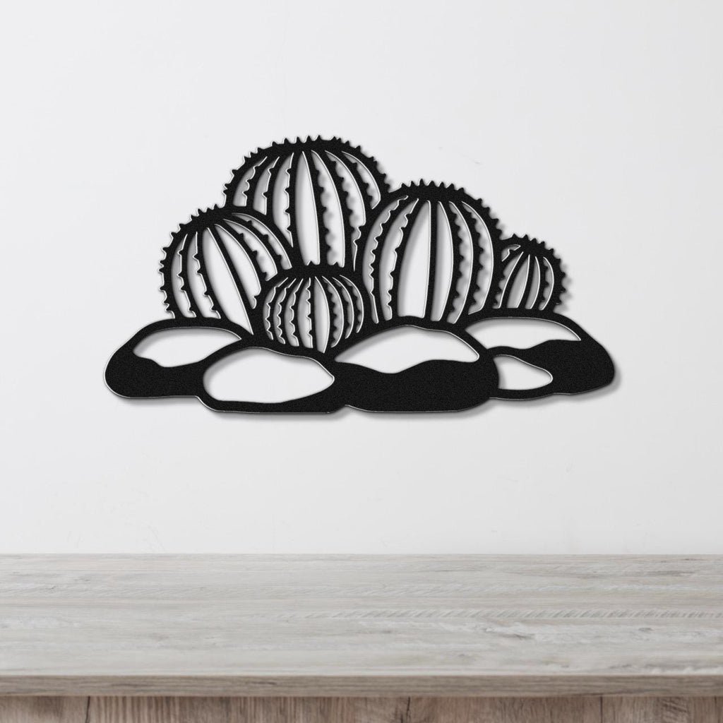 Black metal barrel cactus wall art with geometric cutouts, mounted on a white wall above a wooden surface.
