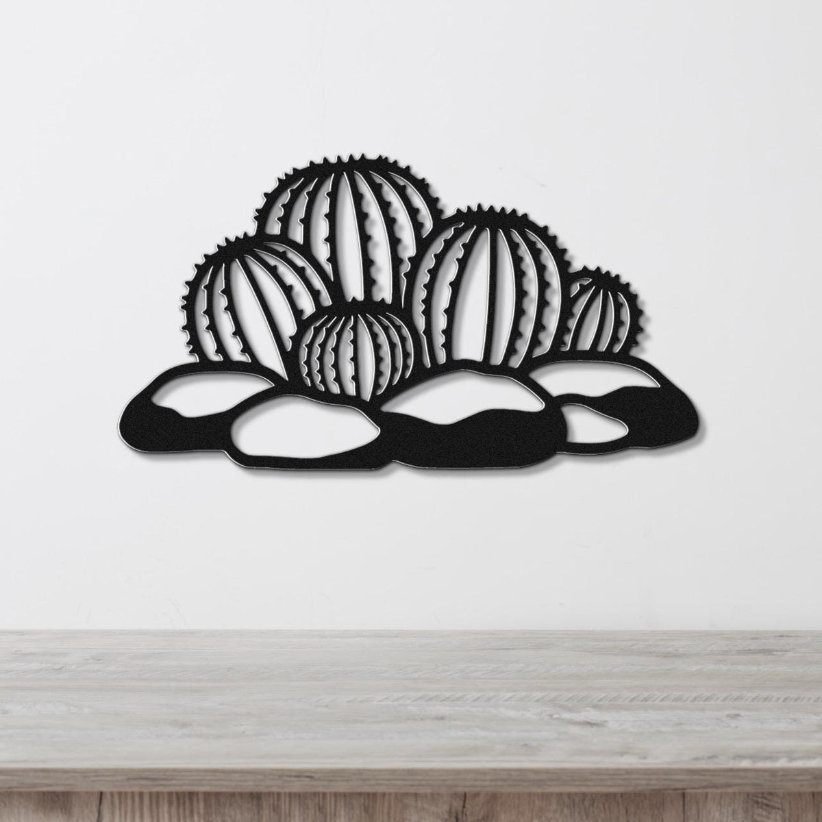Black metal barrel cactus wall art with geometric cutouts, mounted on a white wall above a wooden surface.