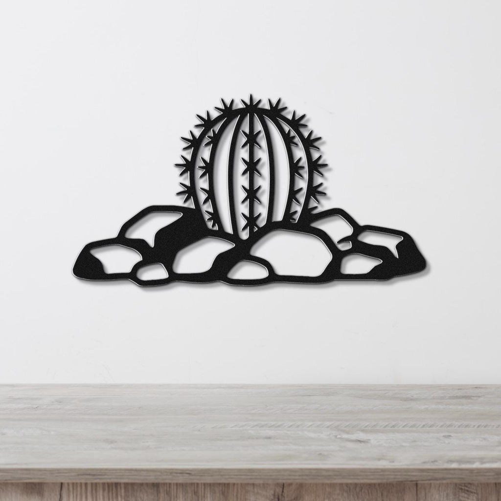 Black metal barrel cactus wall art with spines and rocks cutout, mounted on a white wall above a wooden counter.