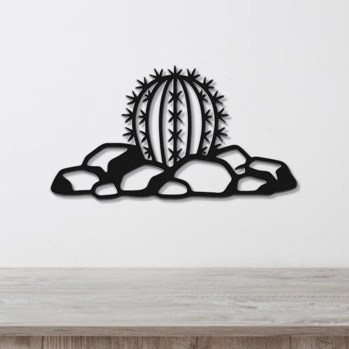 Black metal barrel cactus wall art with spines and rocks cutout, mounted on a white wall above a wooden counter.