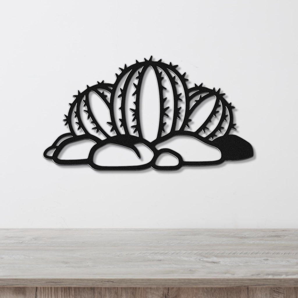 Black metal barrel cactus wall art with spines and cutout details, mounted on a white wall above a wooden surface.