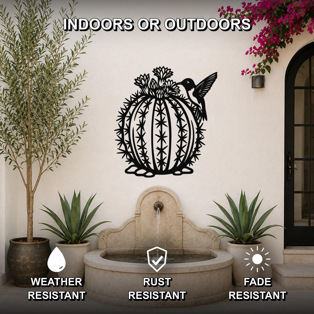 Black metal barrel cactus wall sculpture with flower and hummingbird cutouts, mounted on a white outdoor wall above a stone fountain.