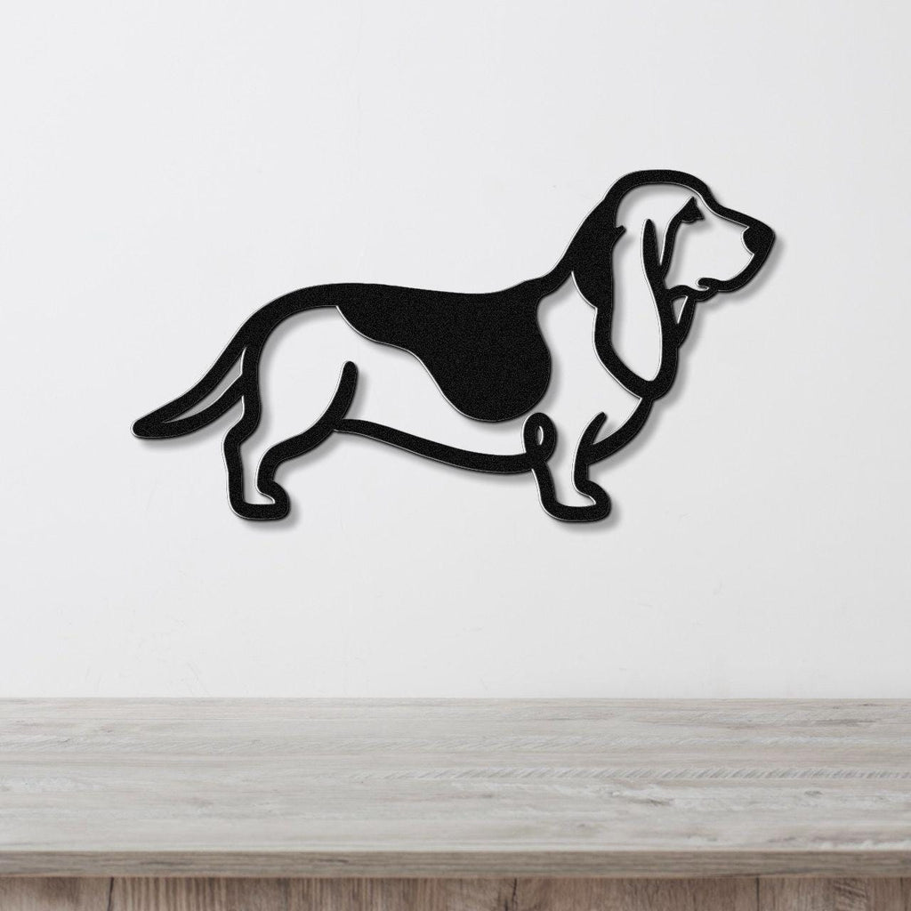 Black metal Basset Hound silhouette wall art with internal cutouts, mounted on a white wall above a light wood surface.