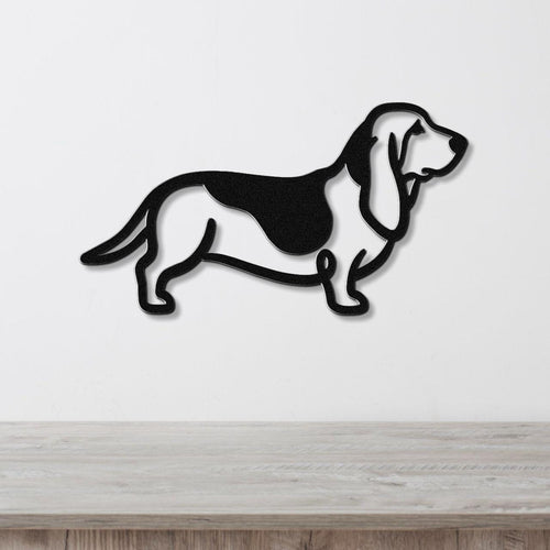 Black metal Basset Hound silhouette wall art with internal cutouts, mounted on a white wall above a light wood surface.