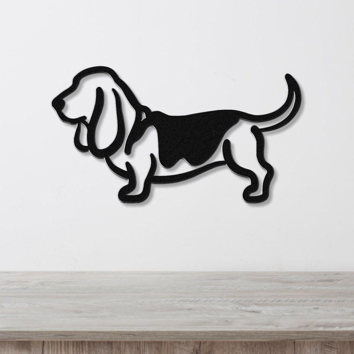 Black metal Basset Hound silhouette wall art with cutout details, mounted on a white wall above a light wood surface.