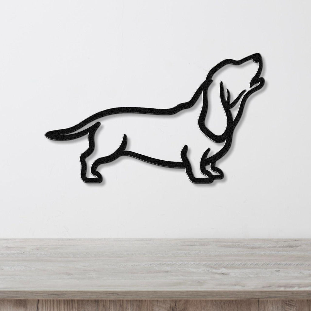 Black metal wall art in a minimalist silhouette of a basset hound, mounted on a white wall above a light wood surface.