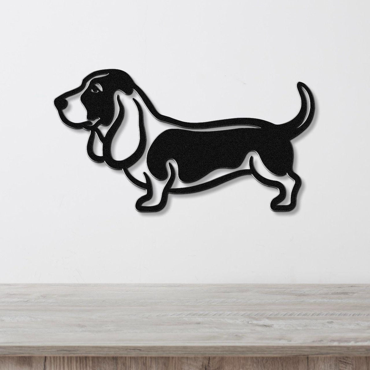 Black metal wall art silhouette of a basset hound, mounted on a white wall above a light wood surface.