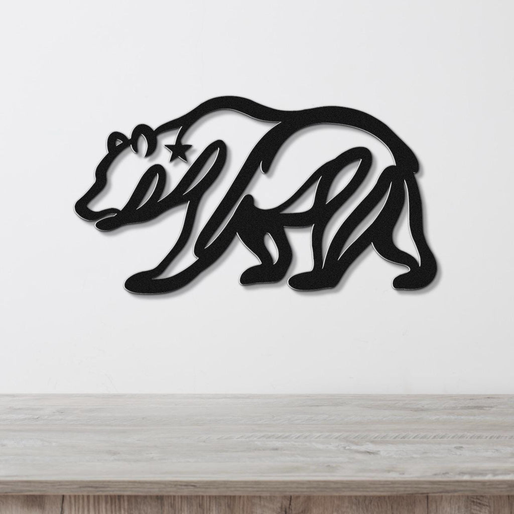 Black metal wall art of a bear silhouette with a star cutout on its shoulder, mounted on a white wall above a wooden surface.