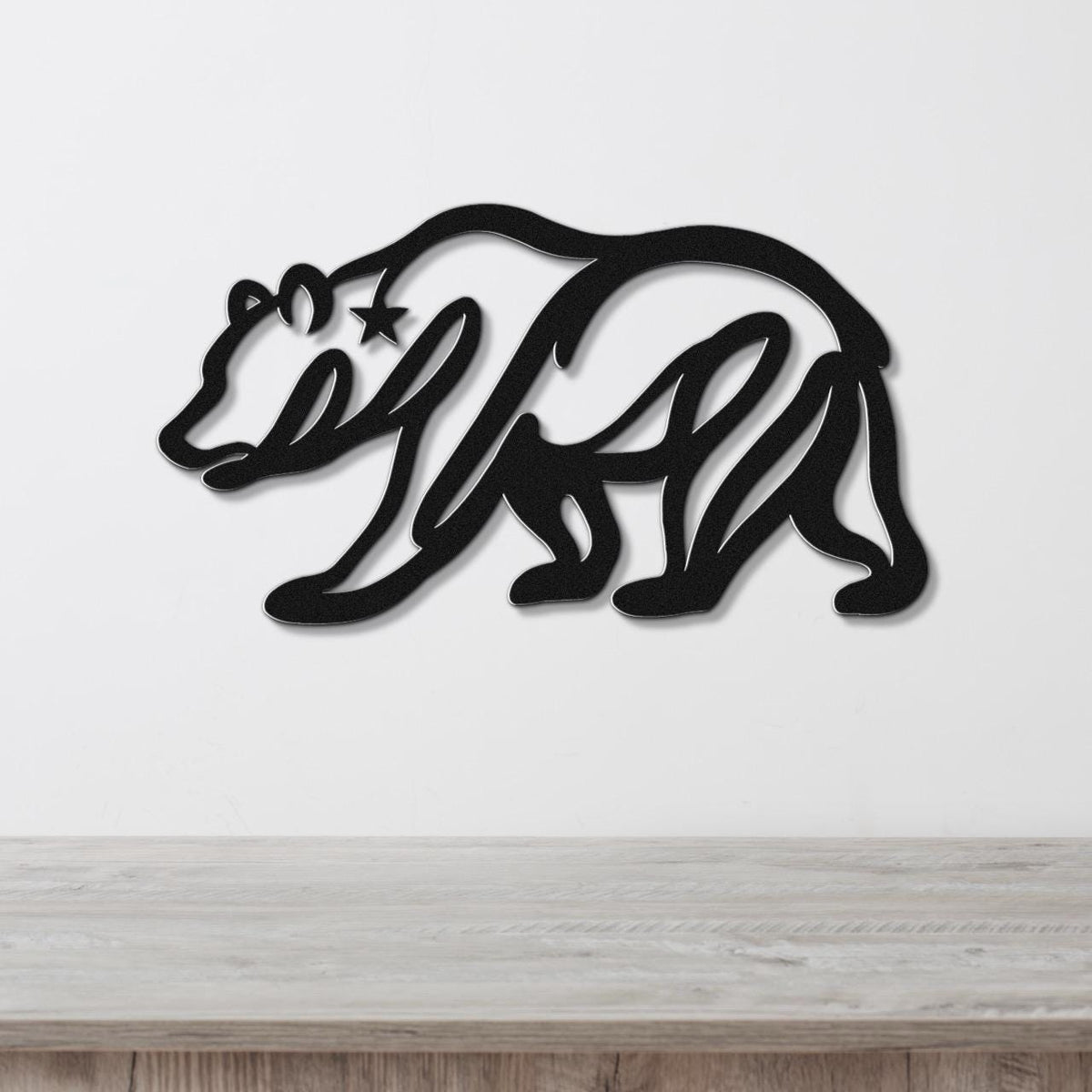Black metal wall art of a bear silhouette with a star cutout on its shoulder, mounted on a white wall above a wooden surface.