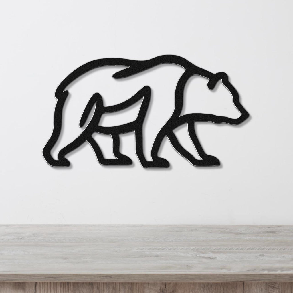 Black metal bear silhouette wall art with internal cutout details, mounted on a white wall above a light wood surface.