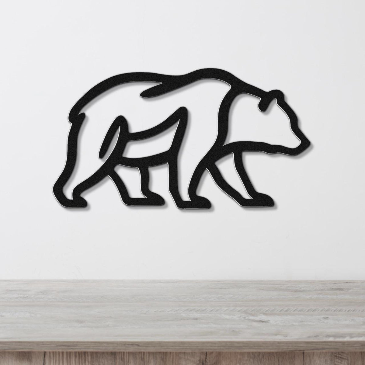 Black metal bear silhouette wall art with internal cutout details, mounted on a white wall above a light wood surface.