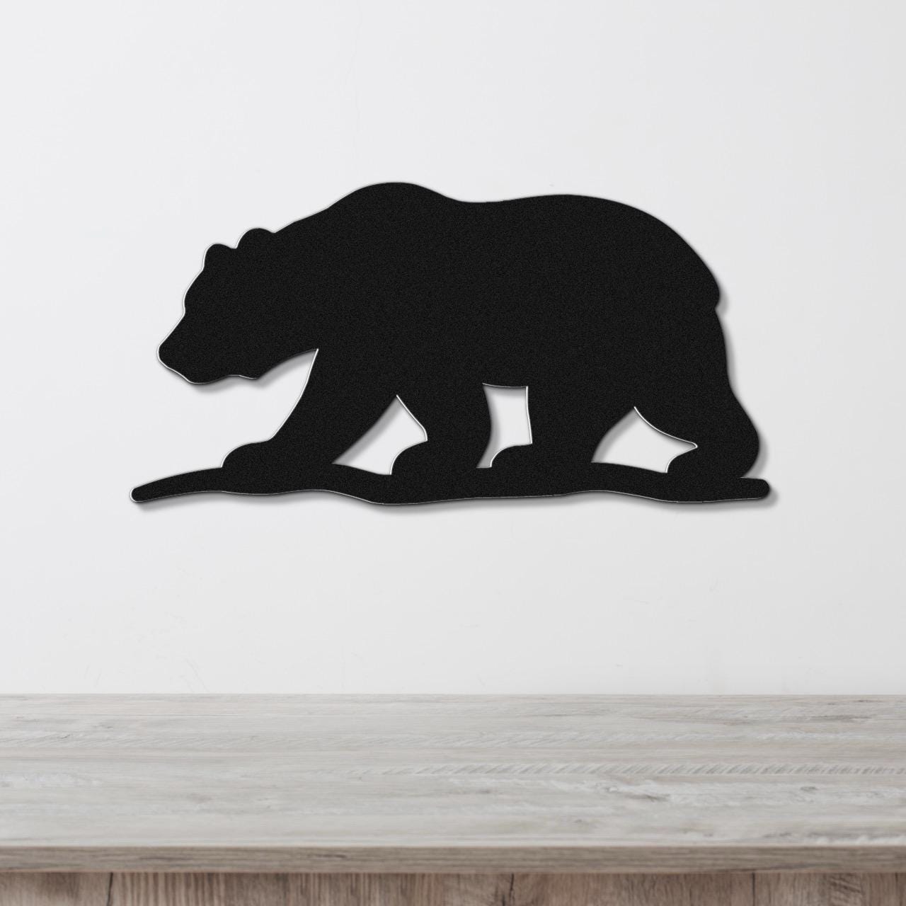 Black metal bear silhouette wall art with cutout legs, mounted on a white wall above a light wood counter.