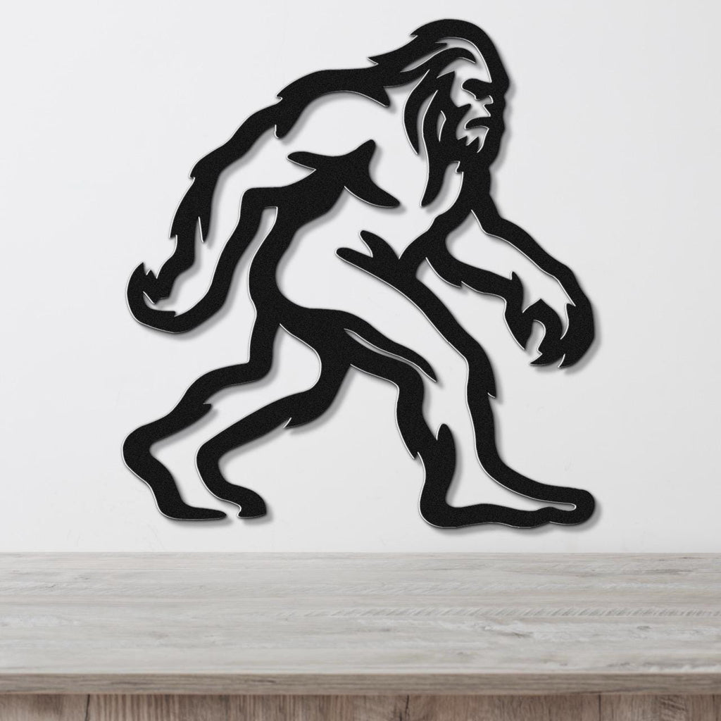 Black metal wall art featuring a rugged Bigfoot silhouette with internal cutout details, mounted on a white wall above a wooden surface.