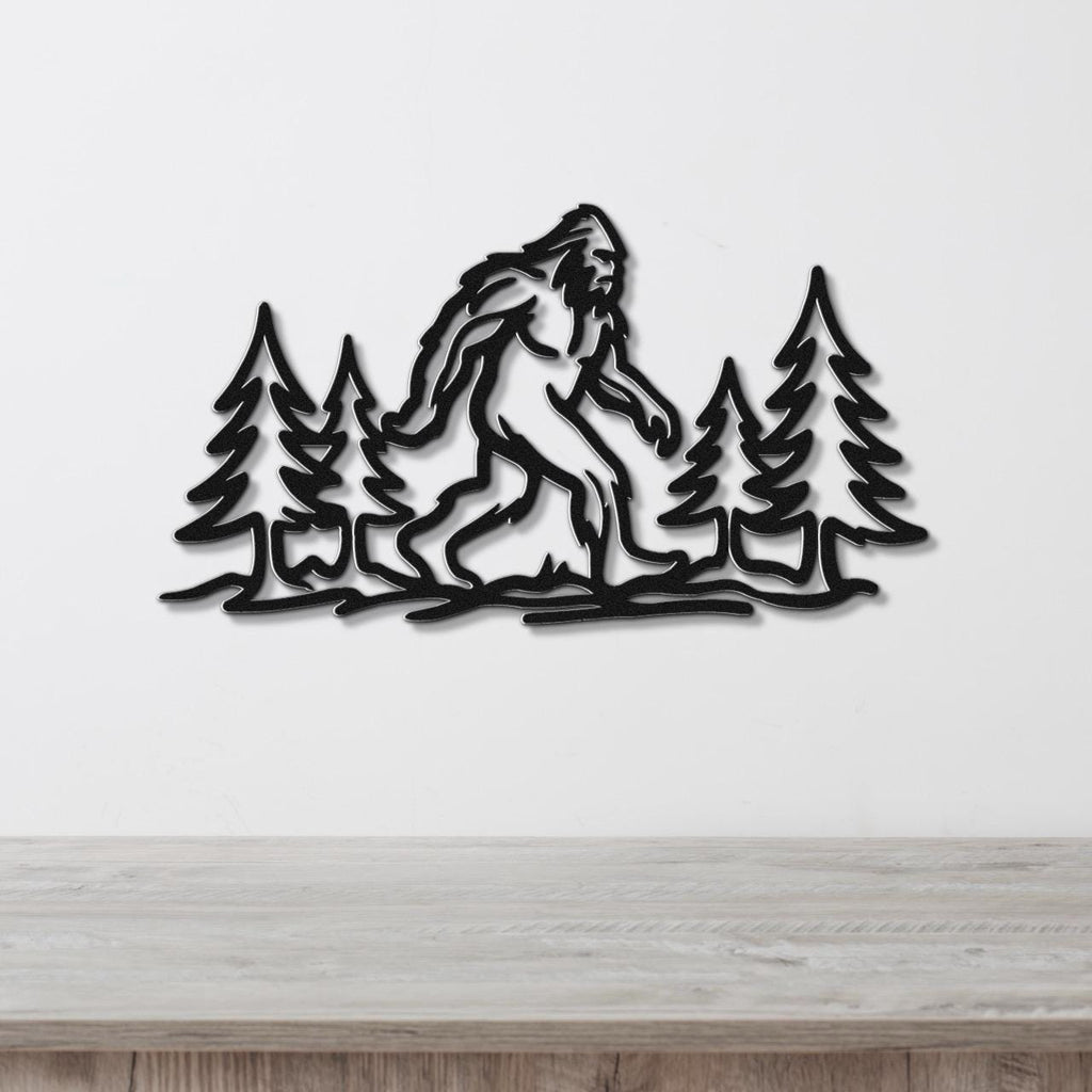 Black metal wall art featuring a Bigfoot silhouette walking through pine trees, mounted on a white wall above a wooden counter.