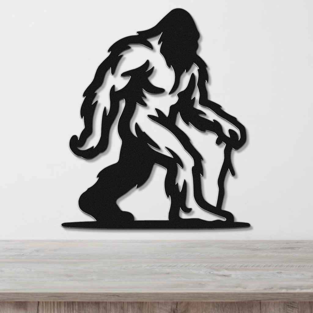 Black metal wall art silhouette of Bigfoot with detailed fur cutouts, mounted on a white wall above a wooden surface.