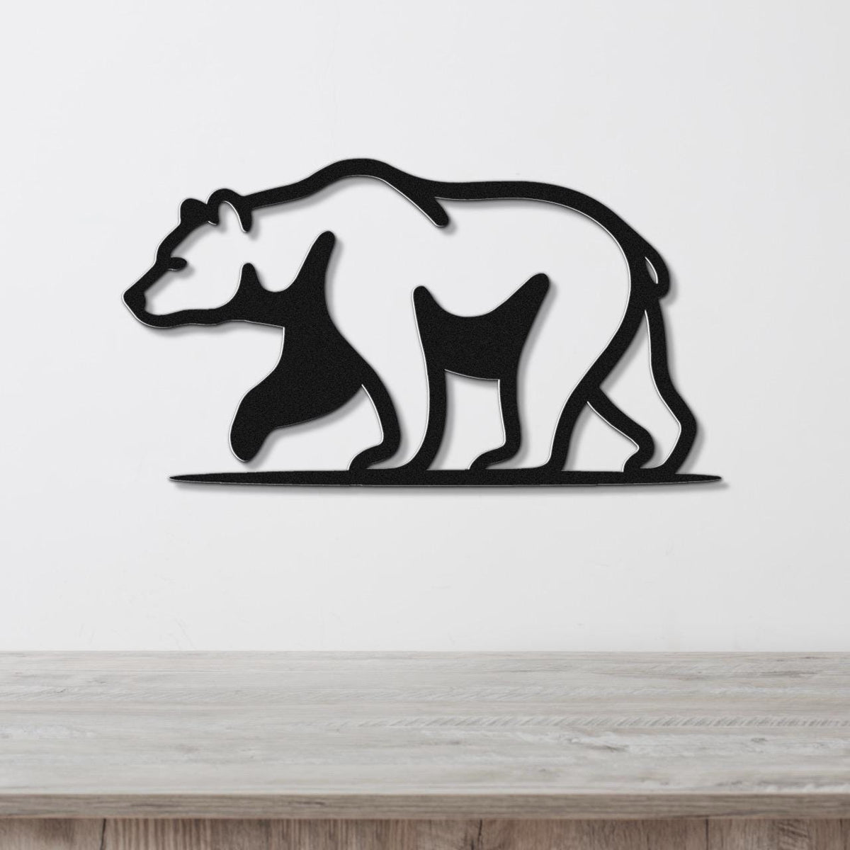 Black metal bear wall art with a silhouette design, mounted on a white wall above a wooden surface.