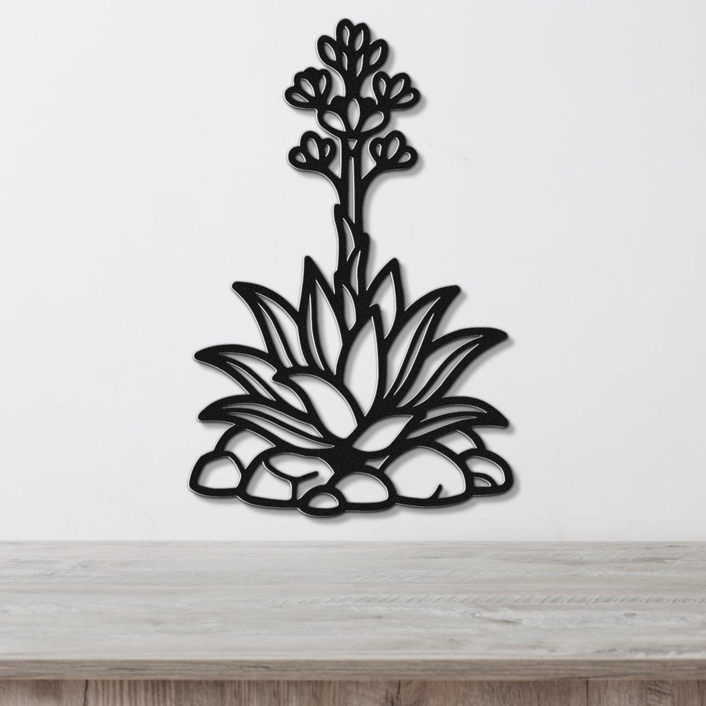 Black metal agave wall art with blooming flower cutout, mounted on a white wall above a wooden surface.