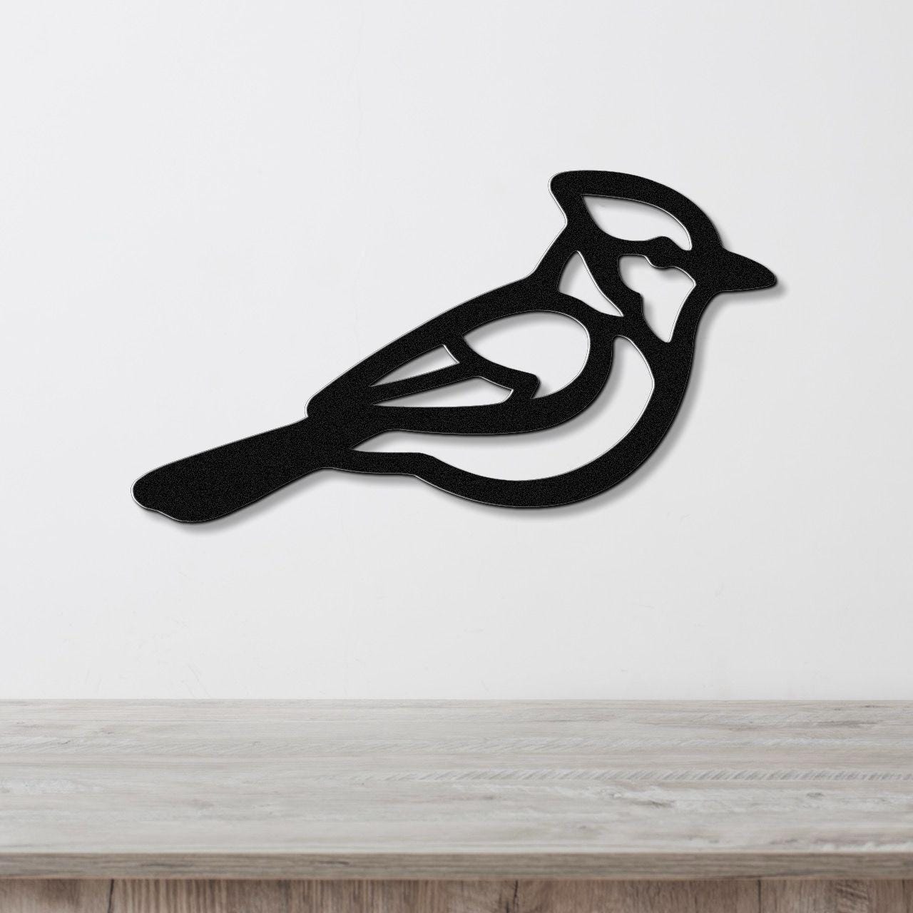 Black metal wall art featuring a cutout silhouette of a blue jay with internal detail, mounted on a white wall above a light wood surface.