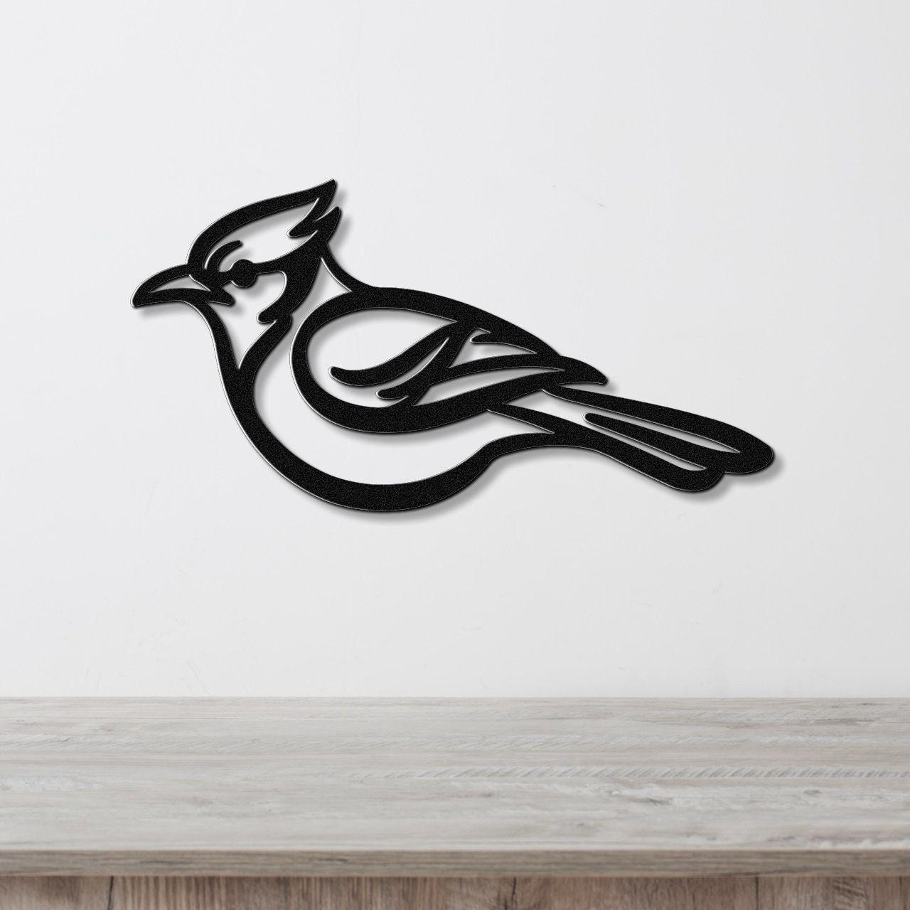 Black metal blue jay wall art with internal feather cutouts, mounted on a white wall above a light wood counter.