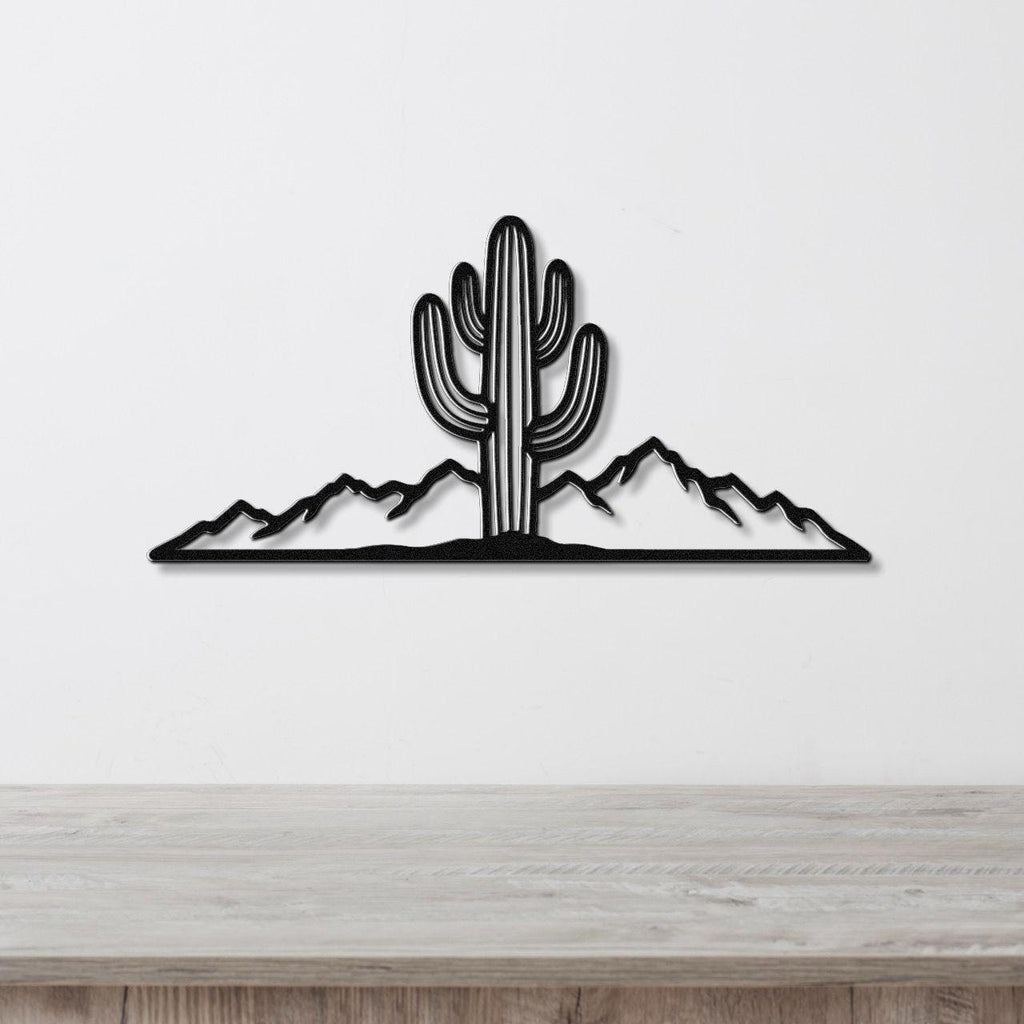 Black metal wall art silhouette of a saguaro cactus and mountain range, mounted on a white wall above a light wood counter.