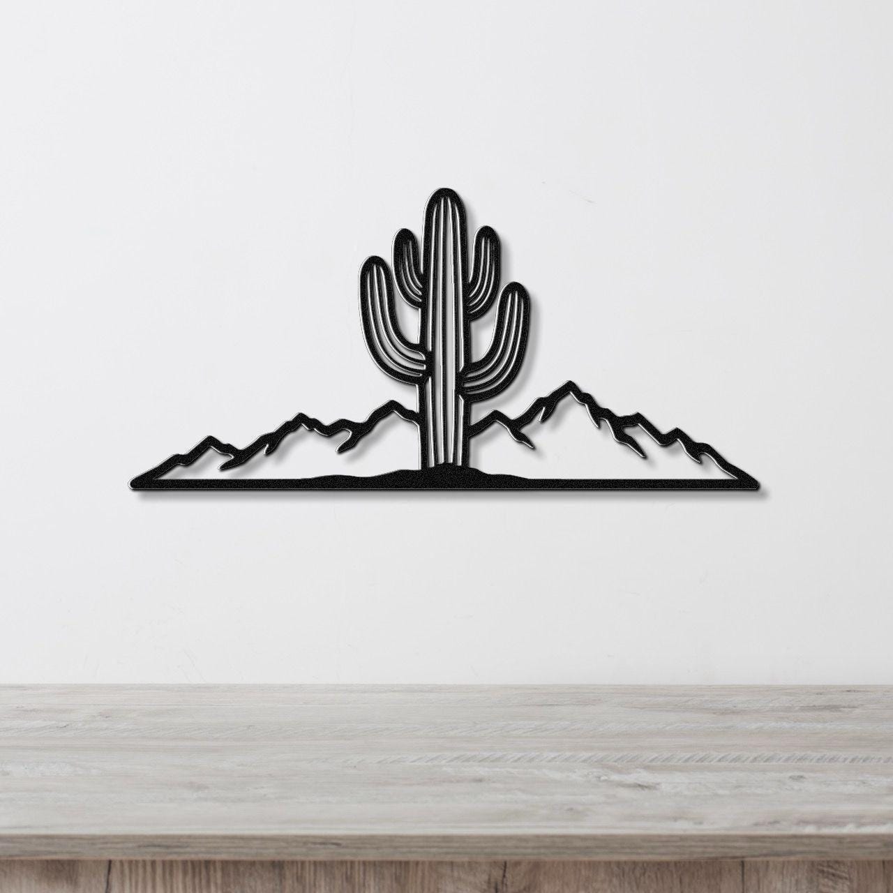 Black metal wall art silhouette of a saguaro cactus and mountain range, mounted on a white wall above a light wood counter.