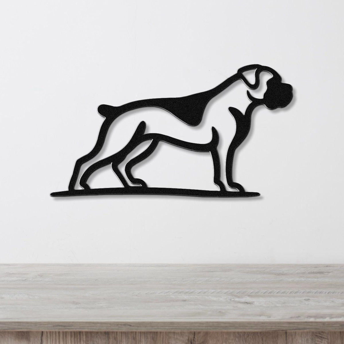 Black metal wall art silhouette of a boxer dog in profile, mounted on a white wall above a light wood surface.