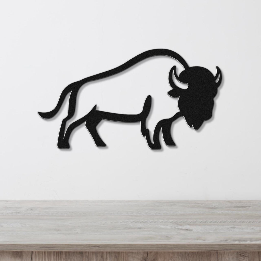 Black metal buffalo wall art silhouette with curved horns and tail, mounted on a white wall above a light wood surface.