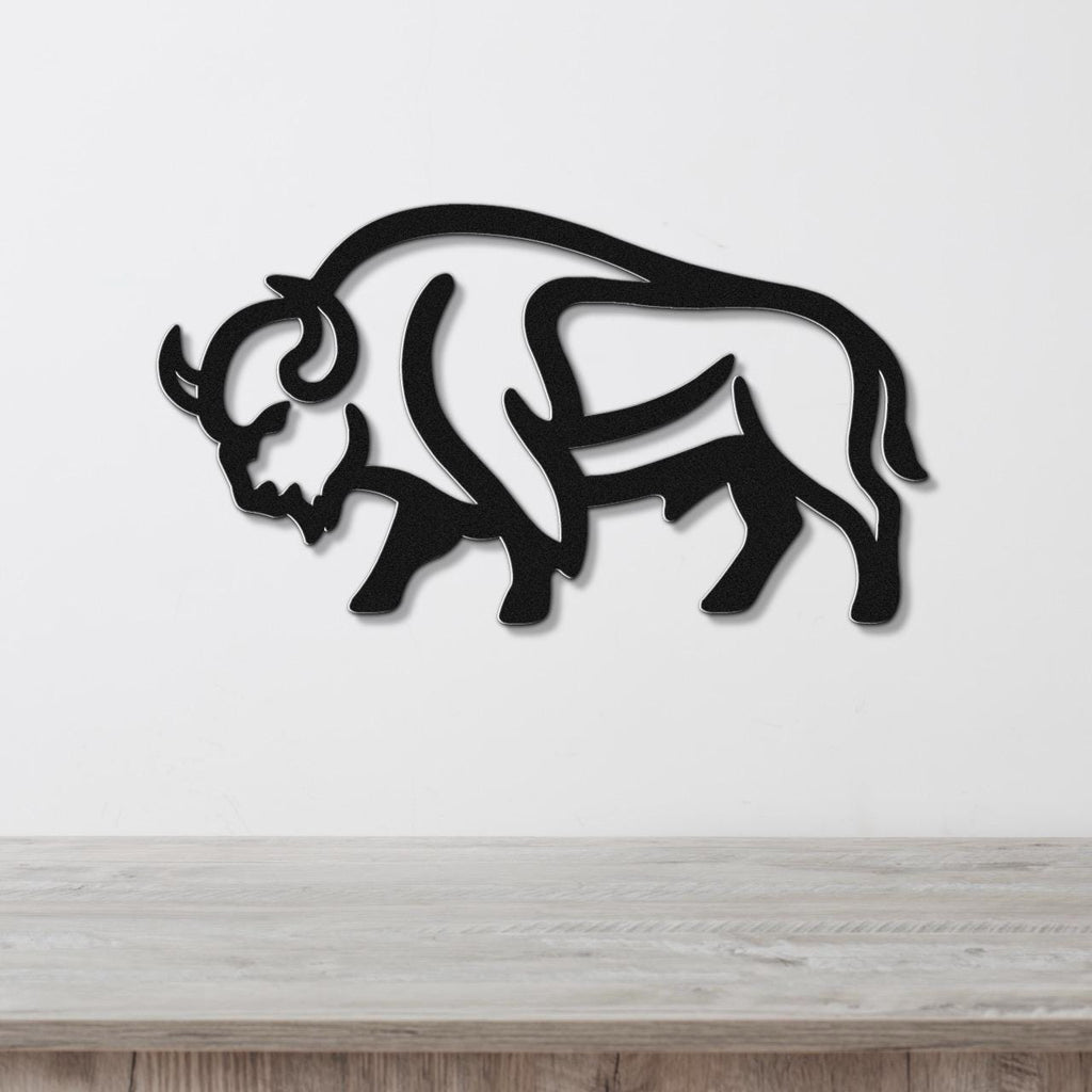 Black metal buffalo wall art with a silhouette cutout design, mounted on a white wall above a light wood counter.